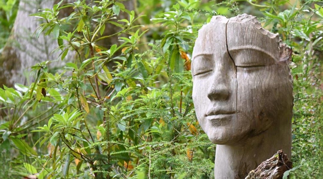Beautiful carved wooden head in the lush green woodland