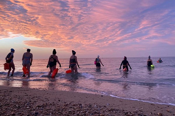 Image of a group of swimmers entering the ocean at sunset
